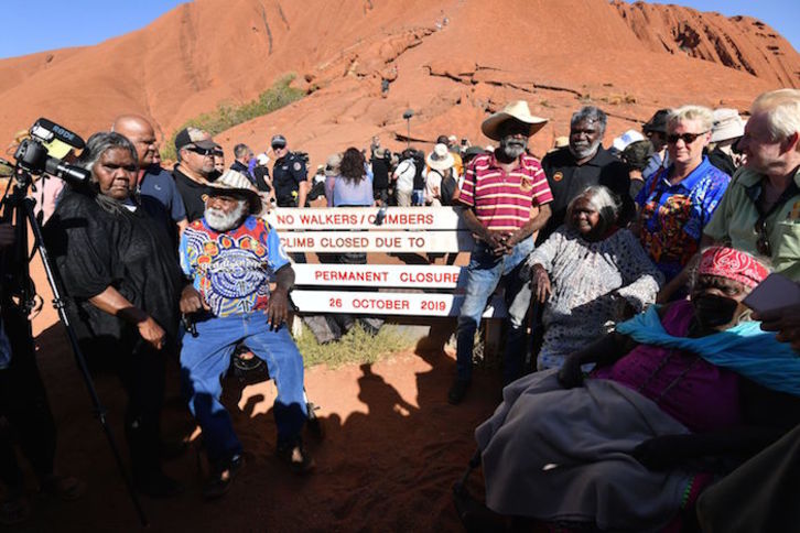 Aborígenes australianos, junto al cartel que anuncia la prohibición de ascender a Uluru. (SAEED KHAN / AFP)