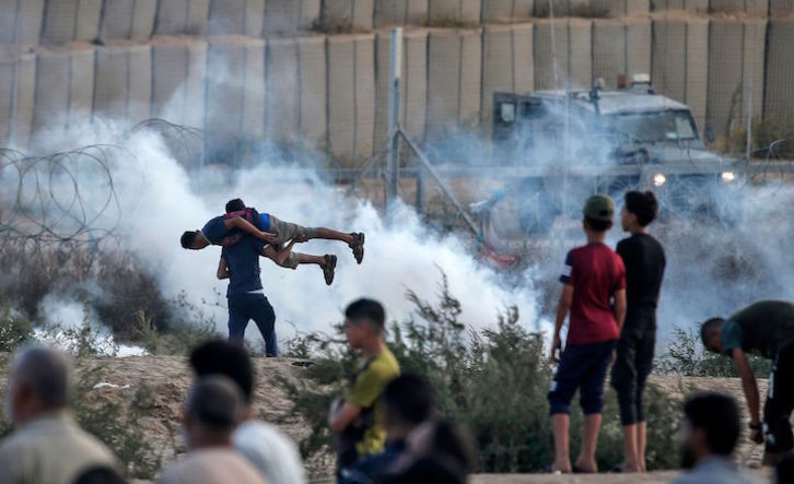 Un hombre traslada a un herido a hombros en Gaza entre los gases lanzados por soldados israelíes.(Mahmud HAMS/AFP)
