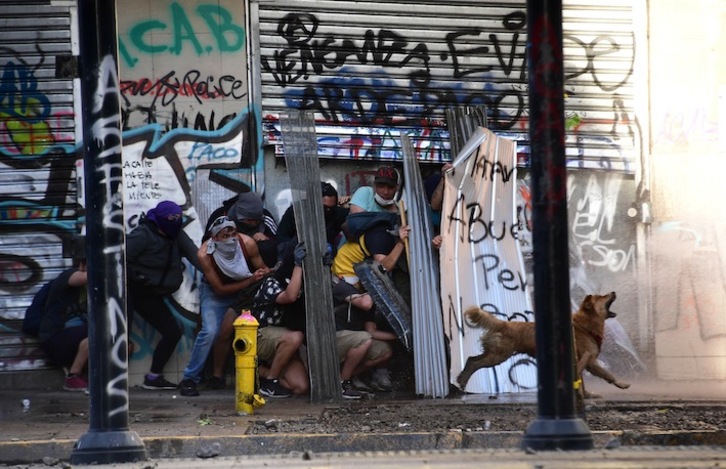 Un grupo de manifestantes se protege del agua a presión lanzada por los agentes antidisturbios. (Martón BERNETTI/AFP)