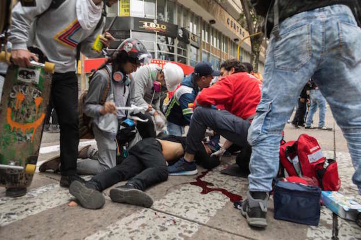Sanitarios y manifestantes ayudan a Dylan Cruz, abatido en el suelo por un artefacto policial. (Camila LASALLE RAMIREZ / AFP) 