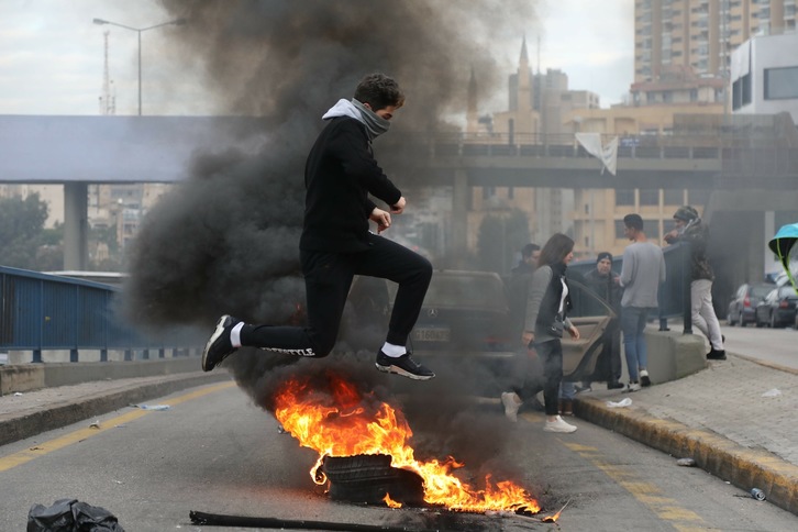 Un  joven salta sobre un neumático ardiendo en una carretera cortada en Beirut. ( IBRAHIM AMRO-AFP)