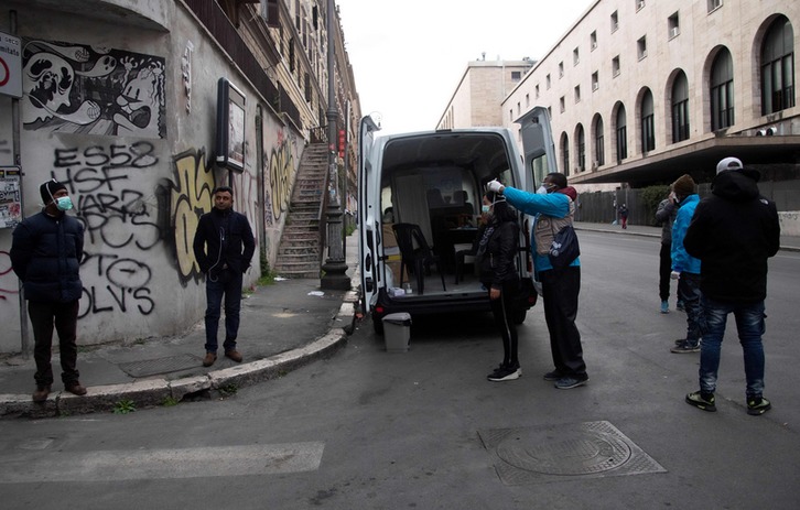 Miembros de una organización humanitaria ayuda a colocarse mascarillas a la ciudadanía en Roma. (Tiziana FABI / AFP)