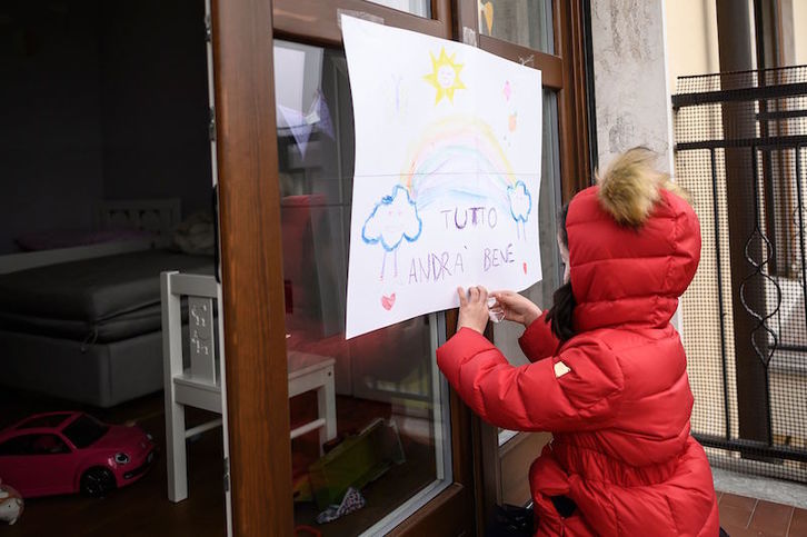 Una niña pega en el balcón de su casa un dibujo hecho ella en la localidad italiana de Manta. (Marco BERTORELLO / AFP)