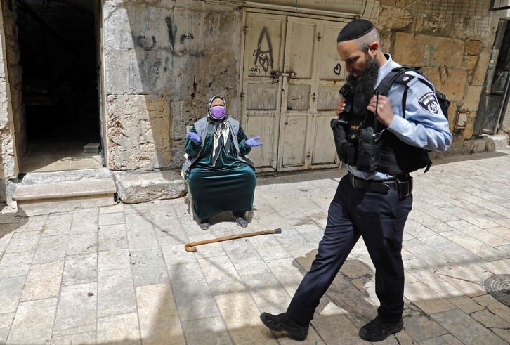 Un policía israelí pasa ante una mujer palestina que reza junto a la Mezquita de Al-Aqsa. (Ahmad GHARABLI/AFP)