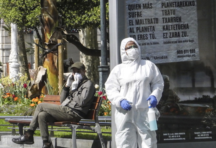 Una mujer desinfecta el Bulebar de Donostia ante un hombre con mascarilla y guantes. (Jagoba MANTEROLA | FOKU)