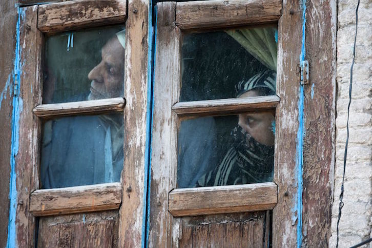 Vecinos de Srinagar, capital de verano de la Cachemira ocupada por India, observan un enfrentamiento armado desde su ventana. (Tauseef MUSTAFA/AFP)