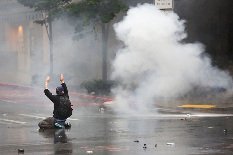 Un manifestante se arrodilla y levanta las manos en Seattle mientras la policía usa gases lacrimógenos en las protestas contra la muerte de George Floyd. (Jason REDMOND/AFP)