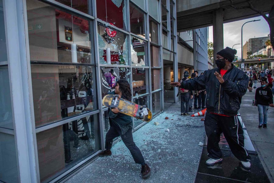 Una manifestante usa un patín para destrozar un restaurante en el centro de Los Ángeles. (Apu GOMES/AFP)
