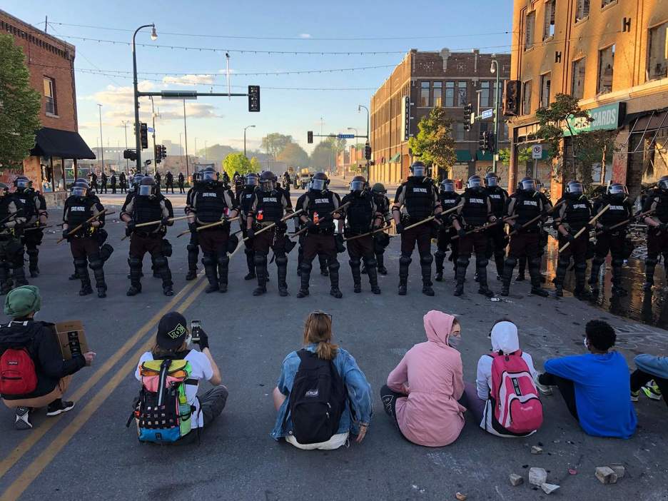 Manifestantes se sientan en la calle frente a una fila de policías durante una protesta en Minneapolis, Minnesota. (Kerem YUCEL/AFP)