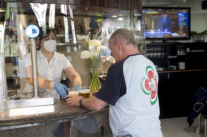 Una camarera atiende tras una pantalla protectora a un cliente de un bar de Iruñea. (Iñigo URIZ/FOKU)