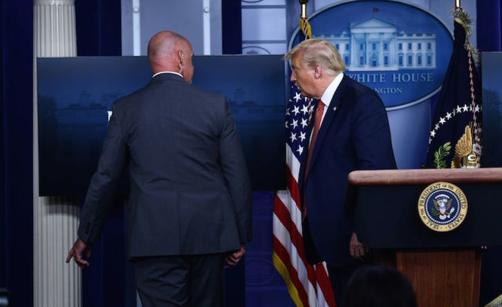 Un miembro de los servicios secretos de EEUU acompaña a Trump a la salida de la sala donde ofrecía la rueda de prensa. (Brendan SMIALOWSKI/AFP)