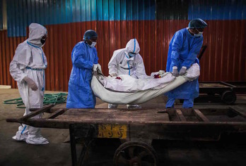 Familiares (vestidos de blanco) y trabajadores de la funeraria preparan a un fallecido por coronavirus para ser incinerado en Nueva Delhi. (Xavier GALIANA/AFP)