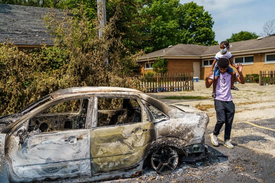 Un hombre pasea con su hija junto a un coche quemado durante las protestas en Kenosha, Wisconsin. (Kerem YUCEL/AFP)