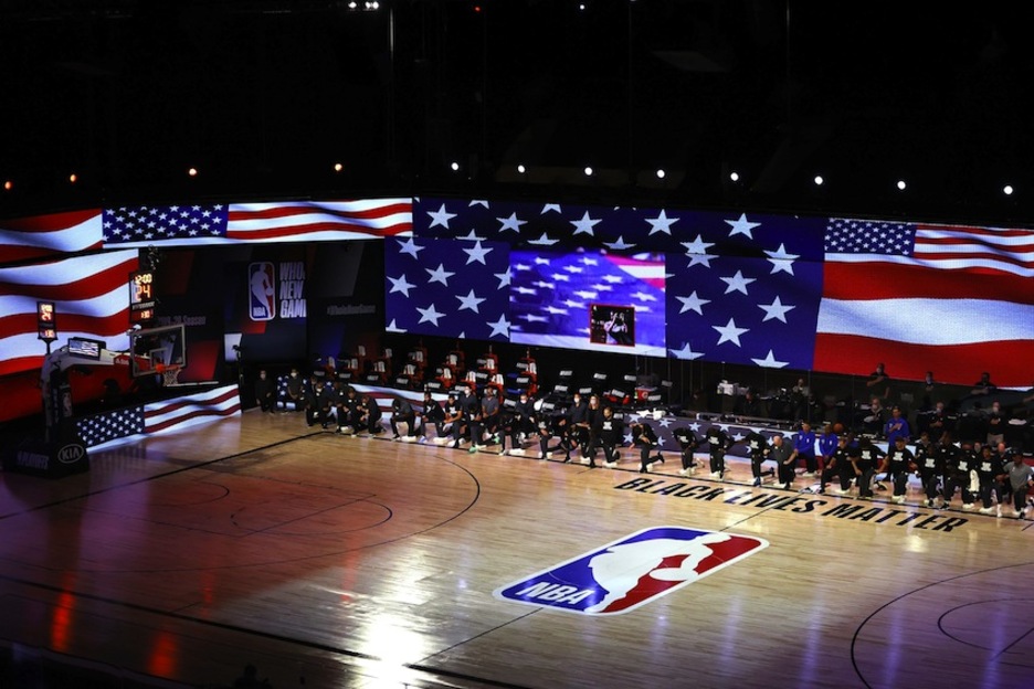 Jugadores y técnicos de los Bucks y los Magic hincan su rodilla en el suelo mientras suena el himno estadounidense antes del tercer partido de la serie de Play-offs. (Mike EHRMANN/AFP)