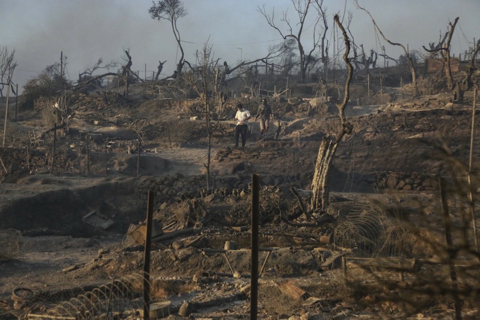Bi gizon kanpalekuko hondakin erreen artean dabiltza. (Manolis LAGOUTARIS/AFP) Bi gizon kanpalekuko hondakin erreen artean dabiltza. (Manolis LAGOUTARIS/AFP)