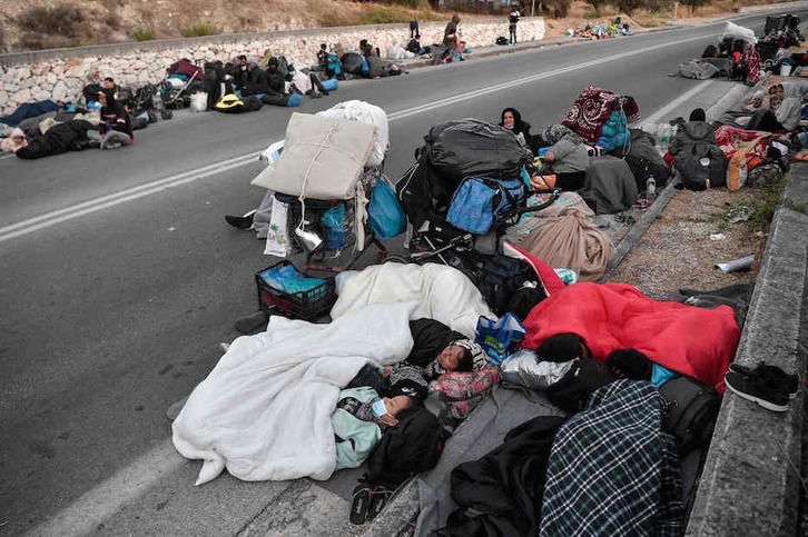 Personas durmiendo sobre el asfalto en la carretera junto al campo de Moria. (Louisa GOULIAMAKI/AFP)