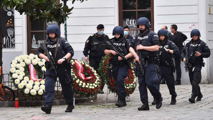 Policías fuertemente pertrechados pasan ante corones de flores depositadas para honrar a las víctimas de Viena. (JOE KLAMAR / AFP)  