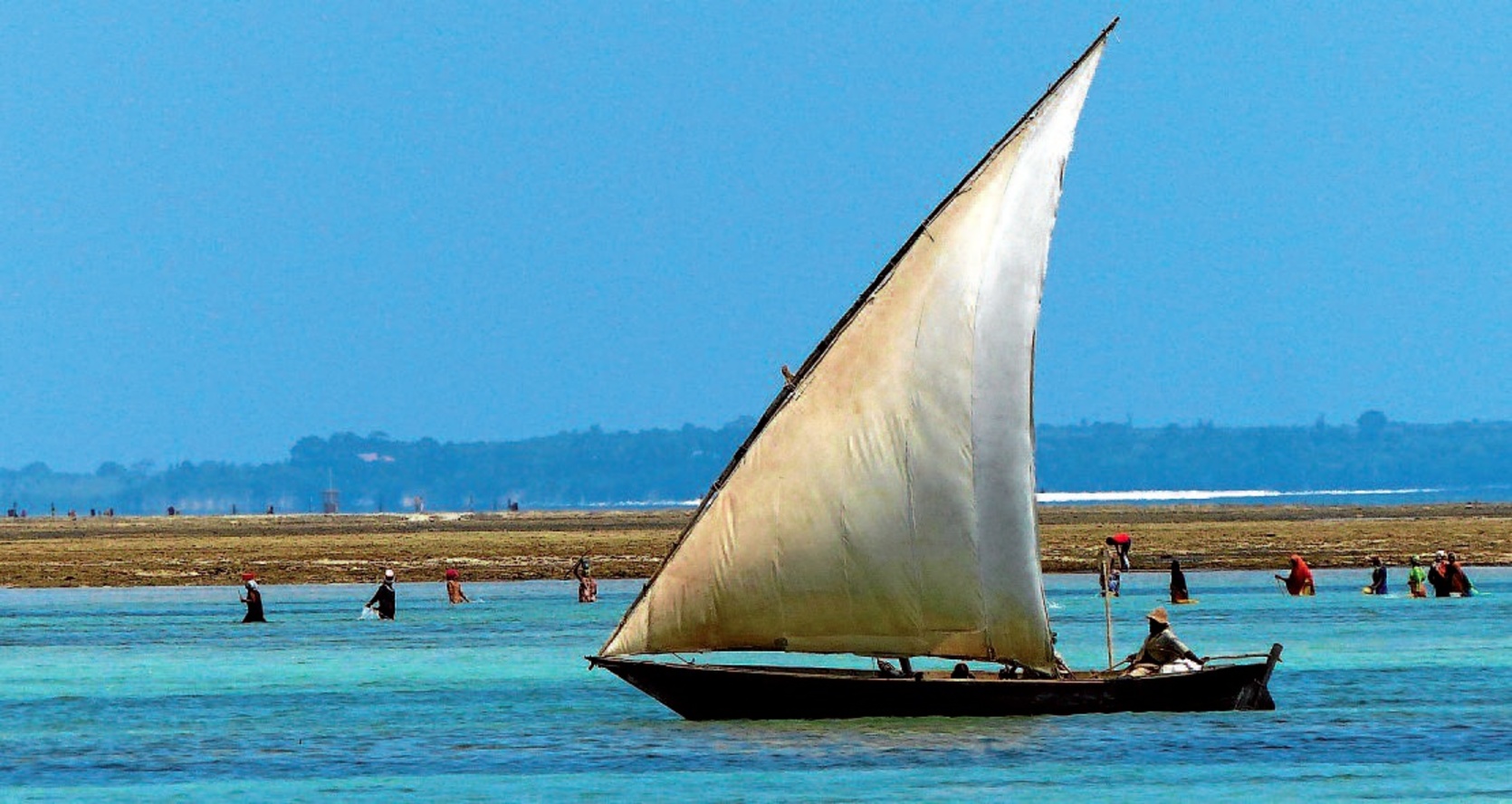 Matemweko hondartza, atzean arrantzalea eta Mnemba atoloia dituela.