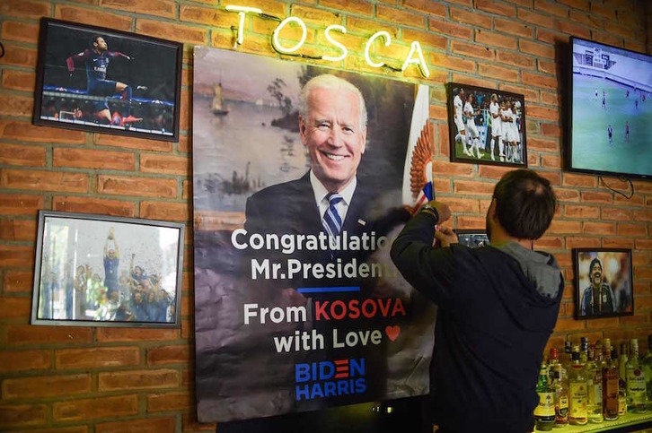 Shkumbin Gashi, propietario de un bar en Rahovec-Orohovac (Kosovo) coloca un poster en el que se felicita a Biden por su victoria. (Armend NIMANI/AFP)