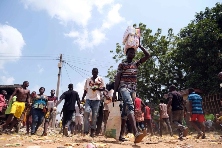 Gente portando comida tras el saqueo masivo de un almacén de alimentos que no se distribuyeron durante el confinamiento por el covid en Abuya, la capital nigeriana. (Kola SULAIMON | AFP) 