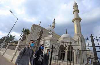 Tres jóvenes palestinos pasan ante una mezquita cerrada en Gaza. (Mahmud HAMS/AFP)