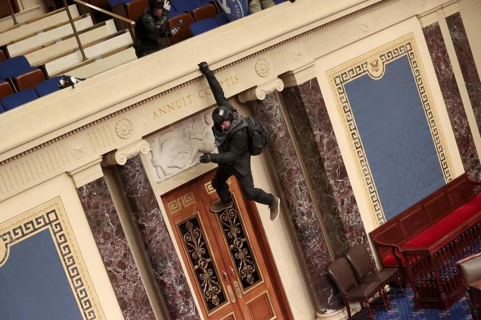 Un manifestante se cuelga del balcón en la Cámara de Representantes. (Win MCNAMEE/AFP)