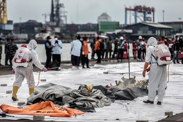 Sanitarios desinfectan bolsas con restos humanos rescatadas del avión accidentado en Indonesia. (Aditya AJI/AFP)