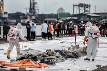 Sanitarios desinfectan bolsas con restos humanos rescatadas del avión accidentado. (Aditya AJI/AFP)