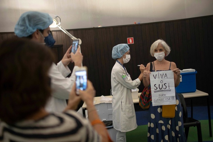 Una mujer se vacuna en Río de Janeiro con un cartel en el que muestra su apoyo al sistema público de salud (SUS) y califica de genocida a Bolsonaro. (Mauro PIMENTEL | AFP)