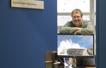 El investigador Gabriel Ibarra, junto a una imagen del dique que acoge las instalaciones de Mutriku para transformar la energía de las olas en energía eléctrica. (UPV/EHU)