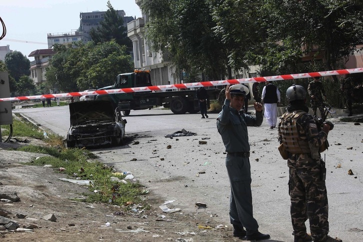 Personal de seguridad al lado de un coche destrozado por los cohetes. (AFP)
