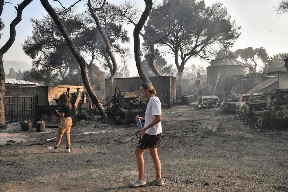 Dos mujeres inspeccionan daños en una instalación de equitación incendiada en Varybombi. (Louisa GOULIAMAKI / AFP)