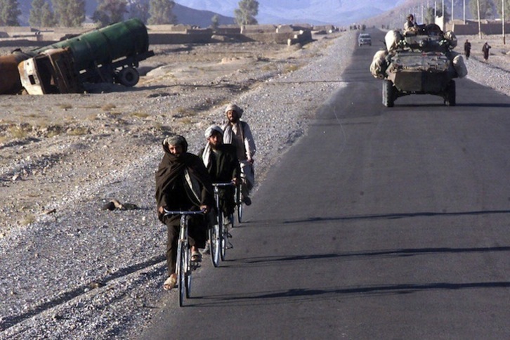 Afganos transitando en bicicleta al paso de un carro blindado estadounidense en Kandahar en 2001. (JOSEPH R. CHENELLY/AFP)