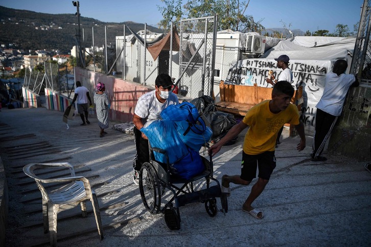 Dos personas transportan sus pertenencias en el viejo campamento de Samos. (Louisa GOULIAMAKI / AFP)
