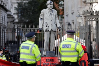 Activistas de Greenpeace organizan una sentada después de instalar una estatua salpicada de petróleo del primer ministro británico Boris Johnson. (Tolga AKMEN/AFP)