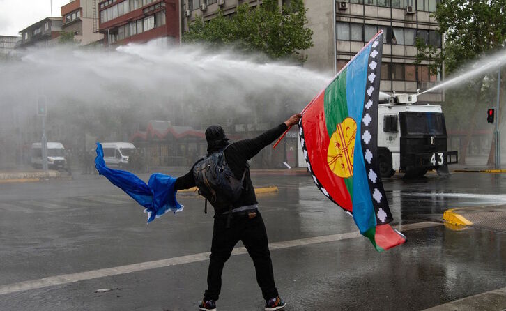 Un manifestante con una bandera mapuche hace frente a los cañones de agua de los Carabineros en Santiago, el pasado fin de semana. (Martin BERNETTI/AFP)