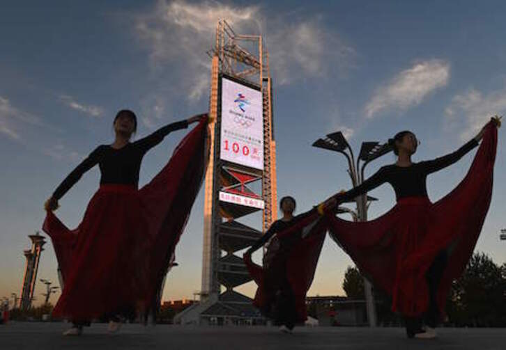 Un grupo de bailarinas danzan junto a un reloj que contabiliza los cien días que restan para el inicio de los Juegos de Invierno de Pekín. (Noel CELIS/AFP)