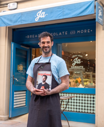 Joseba Arguiñano, bere jaioterrian duen gozo-dendaren kanpoaldean, liburua eskuan.