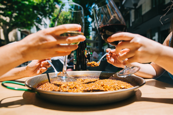 Un brindis con dos copas de vino mientras se come una paella.