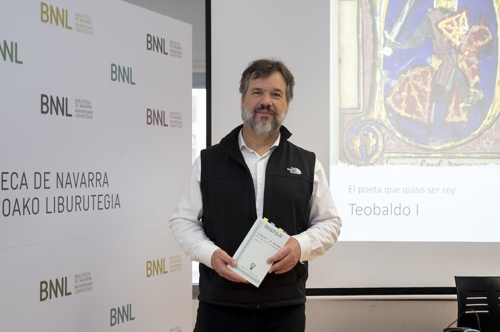 Xabier Irujo posa con su nuevo libro, con una imagen de época de Teobaldo I de Nafarroa al fondo.