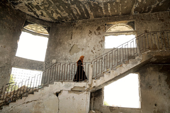Una mujer yemení camina por un edificio dañado por proyectiles.