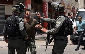 Un guardia de fronteras israelí rocía gas pimienta a un manifestante palestino.