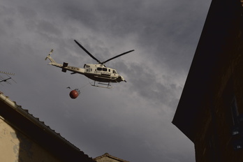 Un helicóptero vuela sobre las viviendas para tratar de sofocar el fuego.
