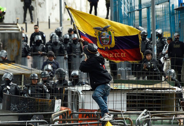 Un manifestante ondea la bandera ecuatoriana ante la sede de la Asamblea Nacional protegida por un importante dispositivo policial.