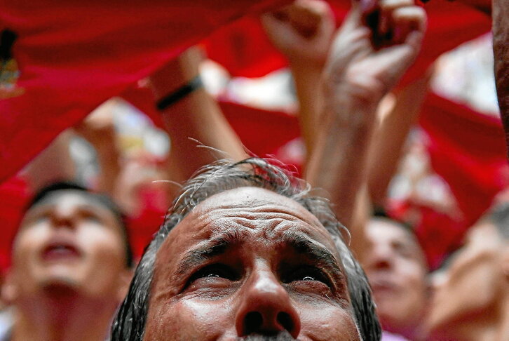 Una encarnación de San Fermín acosada por sus fans. Abajo, mozas bailando bajo la lluvia. A su lado, despliegue de reivindicaciones y pañuelos en alto antes de que vuele el txupinazo.