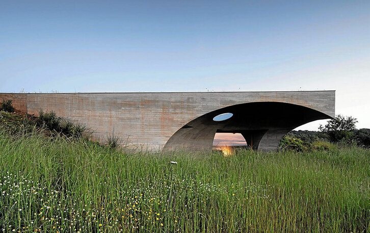 La vivienda se sitúa en la costa del lago Alqueva, de forma semienterrada, aprovechando la pendiente de la colina. Así, el paisaje parece inalterado.