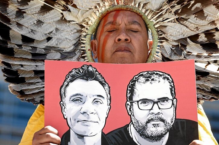 Ekintzaile indigena bat, Pereira eta Phillipsen aurpegiak erakusten dituen kartelari eusten. 