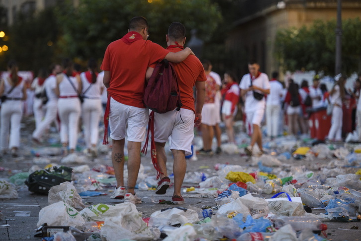 Dos personas pasean por las calles de Iruñea, llenas de residuos tras una jornada de fiesta. 
