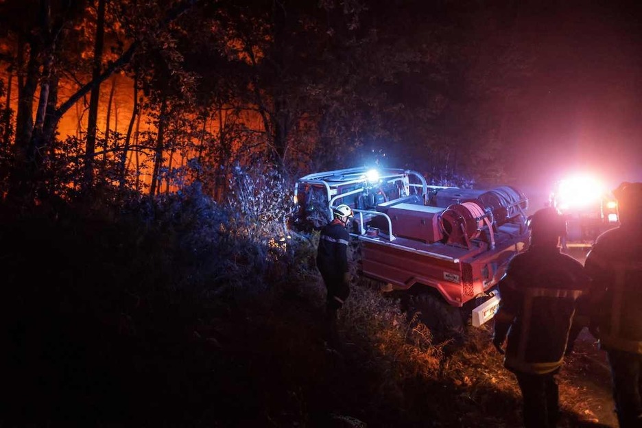 Un grupo de bomberos intenta avanzar hasta el fuego.