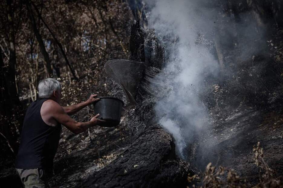 Una persona colabora en la lucha contra el fuego con un balde de agua.
